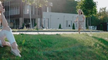 Küçük kız annesine koşuyor çimlerin üzerinde oturuyor, ona sarılıyor ve gülümsüyor.