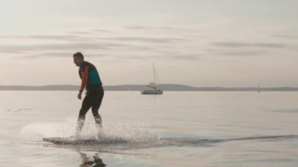El hombre cabalga y cae de la tabla de surf del hidroplano en el lago grande en el atardecer dorado — Vídeo de stock