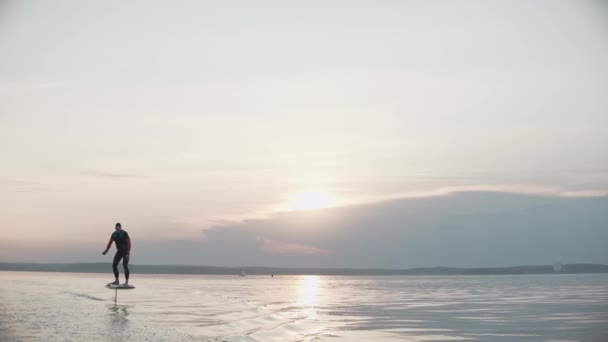 Mann reitet auf Tragflügelboot-Surfbrett auf großem See bei goldenem Sonnenuntergang — Stockvideo