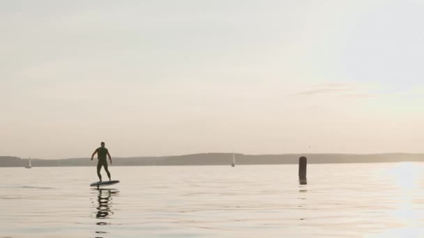 Ο άνθρωπος ιππεύει σε μια σανίδα του σερφ σε μια μεγάλη λίμνη στο χρυσό ηλιοβασίλεμα — Αρχείο Βίντεο