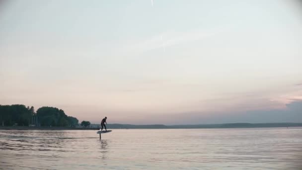 Uomo a cavallo su una tavola da surf aliscafo su grande lago al tramonto rosa e blu — Video Stock