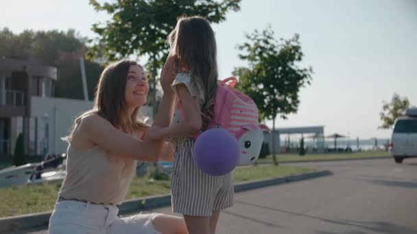 En smilende kvinne kysser og klemmer med datter nær barneleiren en solskinnsdag – stockvideo