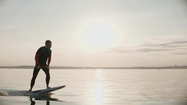 Чоловік їде на дошці для серфінгу на великому озері на золотому заході сонця — стокове відео