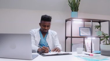 Siyah adam tıbbi notlar yazıyor ve resepsiyonda içki içiyor. 