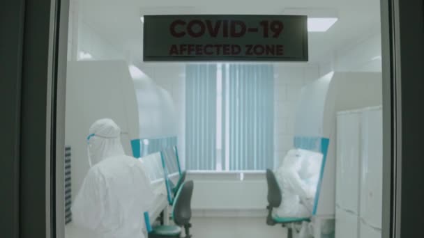 Petugas medis yang memakai baju pelindung dan masker bekerja di laboratorium jelas, melihat dari pintu — Stok Video