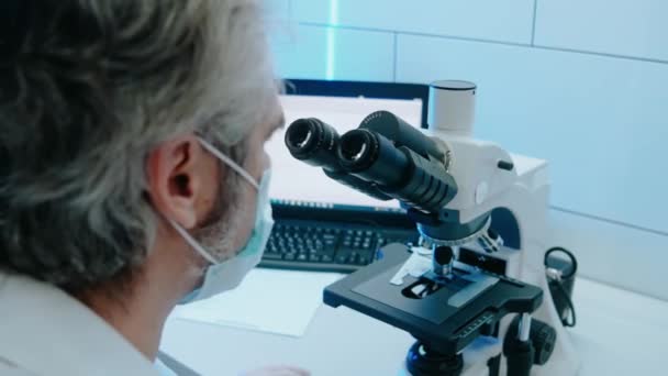 Assistant de laboratoire regarde à travers un microscope dans un laboratoire lumineux blanc — Video