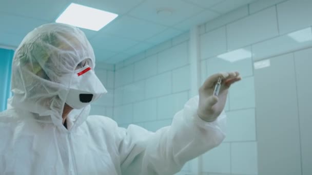 Вчений у захисному костюмі тримає пробірку на світлі в лабораторії — стокове відео