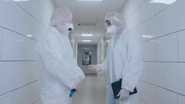 Médicos em trajes de proteção e máscaras conversam no salão do hospital branco brilhante, — Vídeo de Stock