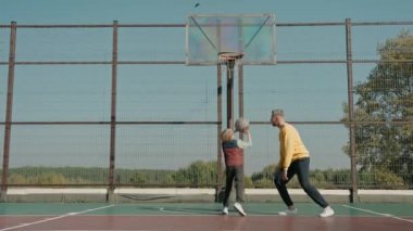 Çocuk güneşli bir günde babasıyla sahada basketbol oynamayı öğreniyor.