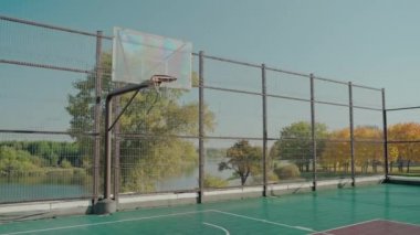 Güneşli bir sonbahar gününde parktaki boş kortta basketbol potası.