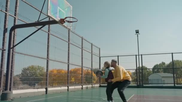 Mann hebt seinen Sohn, um an einem sonnigen Tag den Ball in den Ring zu werfen — Stockvideo