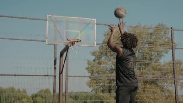 Mann trainiert Basketballwerfen in Korb auf einem Straßenplatz an einem sonnigen Tag — Stockvideo