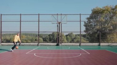 Güneşli bir günde, bir sokak kortunda basketbol topunu sepete atan bir adam.
