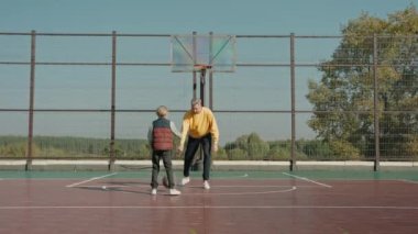Güneşli bir günde basketbol sahasında babasıyla top oynayan bir çocuk.