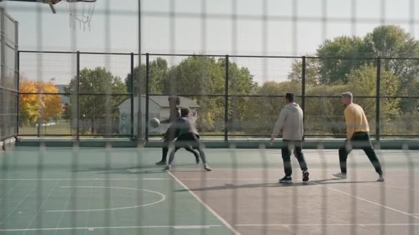 Tiro de quatro homens jogando streetball em uma quadra no parque, retirado da cerca treliçada — Vídeo de Stock