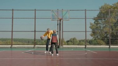 Baba oğluna güneşli bir günde sahada basketbol oynamayı öğretiyor.