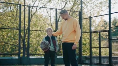 Babam güneşli bir günde basketbol sahasında konuşurken kolunu oğlunun omzuna koyar.