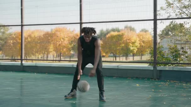 Czarny człowiek dryblowanie koszykówka na boisku w w parku i patrzy w aparat — Wideo stockowe