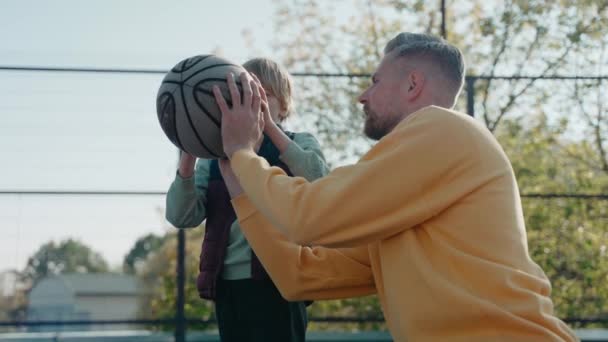 Vater bringt Sohn bei, wie man einen Basketballball auf einem Platz hält und wirft — Stockvideo