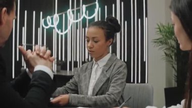Kadın, modern gri ofis odasındaki iş arkadaşlarıyla bir toplantı hakkında bilgi veriyor.