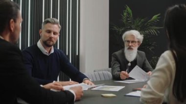 Takım elbiseli bir işadamı toplantıda oturan meslektaşları veya ortaklarıyla konuşuyor