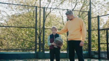 Baba güneşli bir günde oğlunu basketbol antrenmanında alkışlıyor.