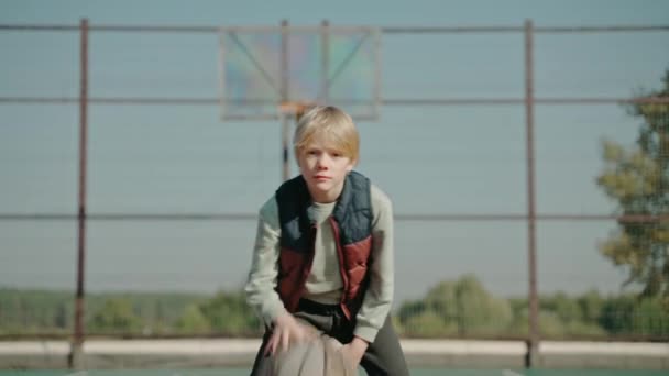 Boy hitting a basketball ball, practicing on a court and looking at the camera — Stock Video