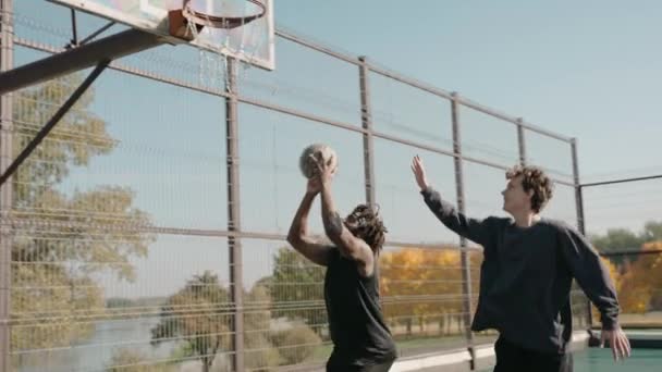 Чернокожий мужчина бьет мяч в корзину, играя в стритбол с друзьями, счастлив победить — стоковое видео