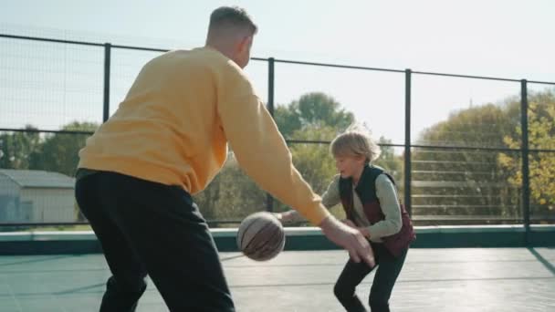 Junge wirft Ball mit Vater auf dem Basketballplatz an einem sonnigen Tag — Stockvideo