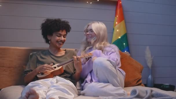 Un cuplu de tineri LGBT se află în pat seara și joacă îmbrățișarea ukulele — Videoclip de stoc