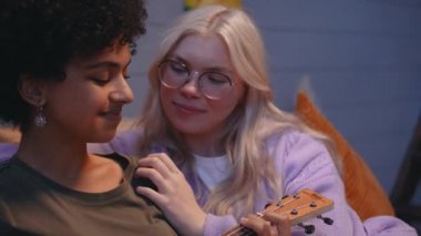 Genç bir LGBT çifti yatakta uzanıp ukulele çalıp öpüşüyor ve gülümsüyor. 