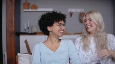 Güzel lezbiyen çift evdeki kanepede oturup birlikte gülüyorlar.