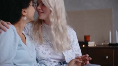 Lezbiyen çift öpüşüyor, gülümsüyor, el ele tutuşuyor, kanepede oturuyor.