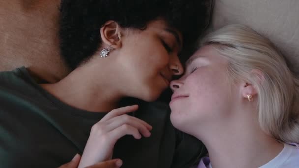 Young lesbian couple kisses laying in bed and smiles, shot from top — Stockvideo