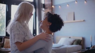 Genç lezbiyen çift dans ediyor ve gülümsüyor, öpüşüyor ve konuşuyor, kanepede oturuyor.