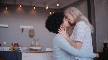 Lezbiyen genç çift öpüşüyor, sarılıyor ve gülümsüyor, kanepede oturuyor.