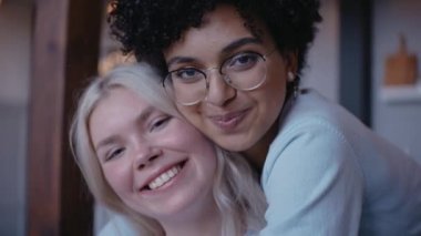 Genç bir kızın, kız arkadaşına arkadan sarılıp kameraya baktığı yakın çekim.