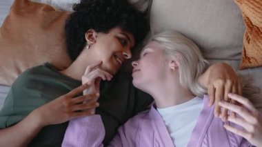 Genç lezbiyen çift yatakta uzanıyor ve gülümsüyor.