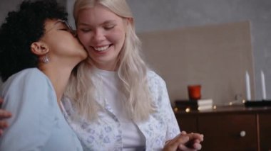 Genç kızlar yanaktan öpüşür ve kanepede otururken gülümser.