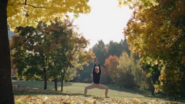 Genç kadın sonbahar parkında yoga minderinde tanrıça yoga pozu veriyor.