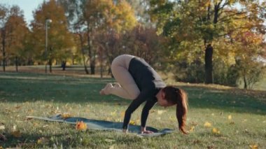 Genç bir kadın aktif yoga yapıyor. Şehir parkında yoga minderinde el ele duruyor.