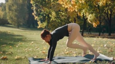 Chaturanga, kobra ve yoga minderiyle parkta kıvrılan genç bir kadın.