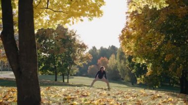 Genç bir kadın, sonbahar parkında yoga minderinde prasarita padottanasana yapıyor.
