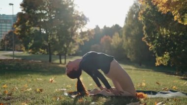 Briç oynayan genç bir kadın sonbahar parkında yoga minderinde poz veriyor.