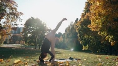 Genç bir kadın, sonbahar parkında yoga pozisyonu alıyor.