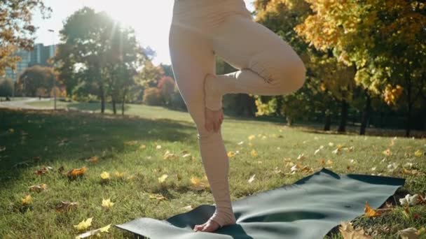 Mladá žena dělá jógu pózovat a táhne se v podzimním městském parku na podložce jógy — Stock video