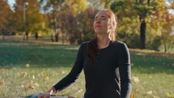 Fiatal nő, akinek a meditáció ül szőnyegen lótuszpozícióban a városi parkban — Stock videók
