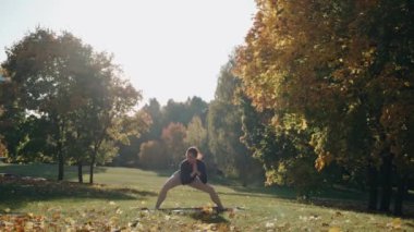 Egzersiz yapan ve sonbahar parkında yoga minderinin üzerinde esneyen genç bir kadın.