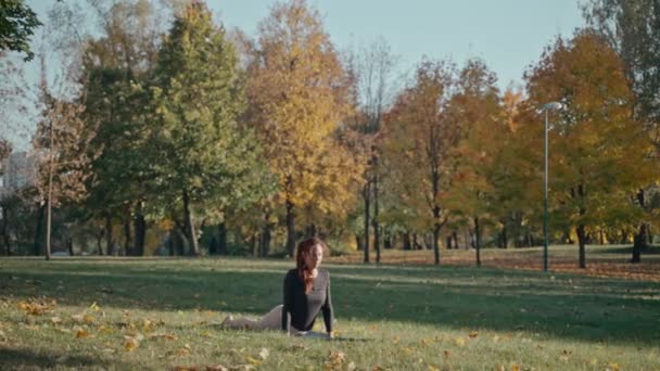 Fiatal nő hátrafelé ível az őszi városi parkban egy jóga szőnyegen egy napsütéses napon — Stock videók