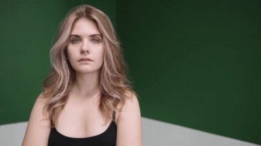 Blonde woman turns from sad to happy smiling, standing in green studio